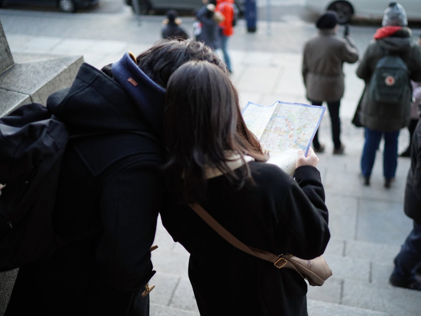 Two people in black jackets standing on a city street trying to figure out how to get from one place to another by using a map.