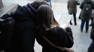 Two people in black jackets standing on a city street trying to figure out how to get from one place to another by using a map.