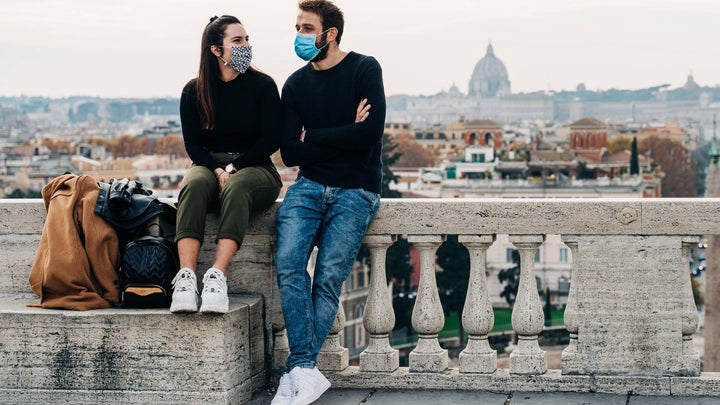 couple resting at a piazza in rome wearing masks and sitting next to their bags
