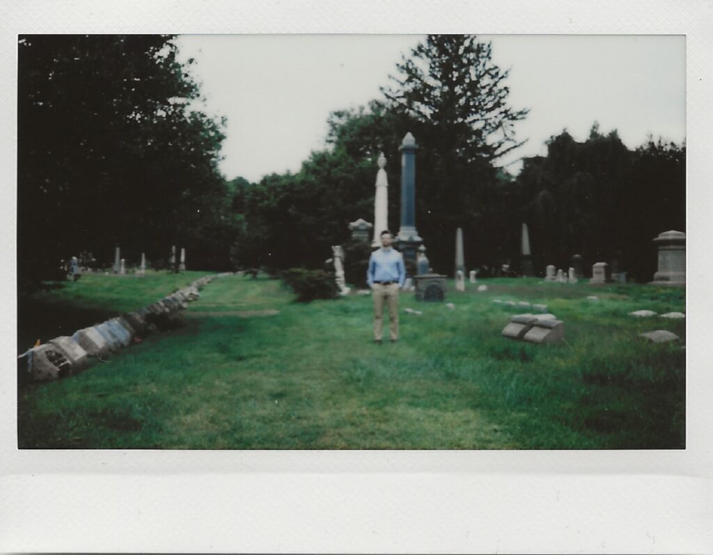 A horticulturist in a blue shirt and khakis staying on the mow line among tall headstones