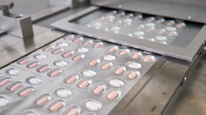 Three white and pink Pfizer COVID antiviral pills in plastic packaging.