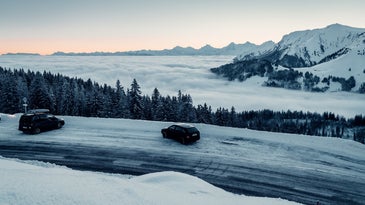 Two black cars on a snowy mountain highway with black ice