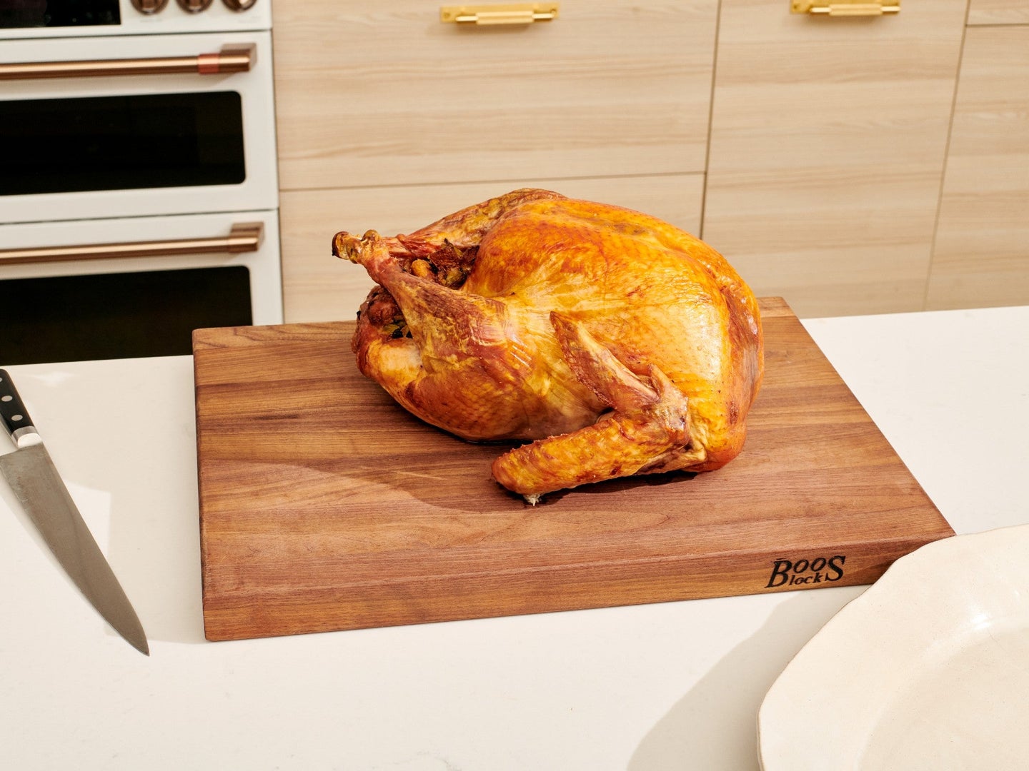 Holiday turkey awaiting carving on a cutting board and white kitchen counter