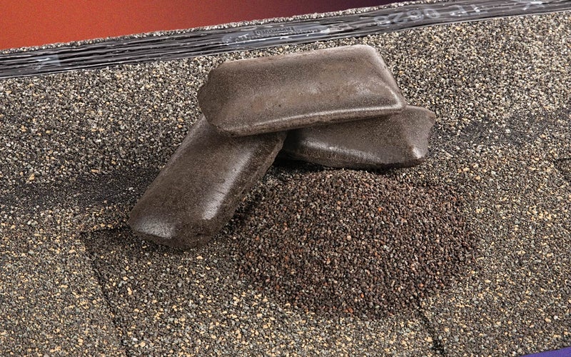 An asphalt shingle with some recycled shingle granules and packed asphalt briquettes on top of it, part of GAF's shingle recycling process.