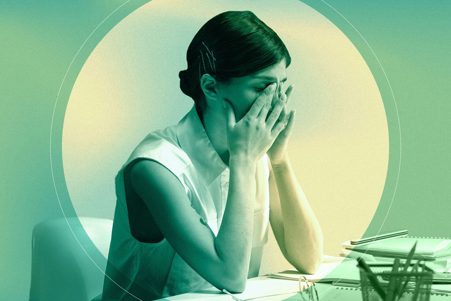 a stressed woman sitting at a desk puts her face in her hands