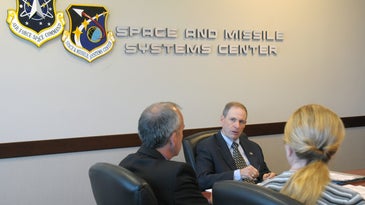 Three Air Force officials sitting around a desk at Space Force Systems Center