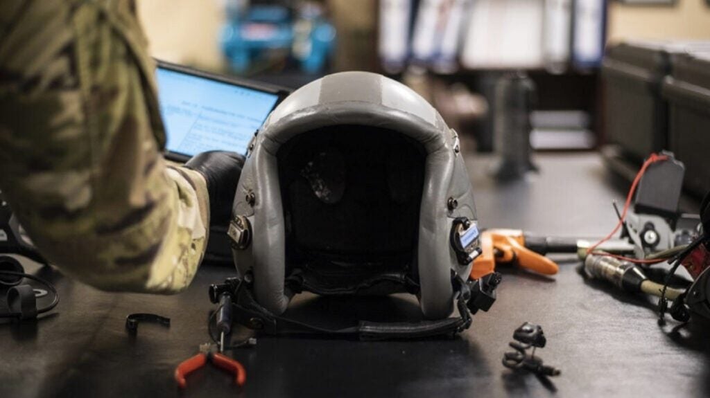 Gray padding from Air Force pilot helmet on a desk next to a laptop and wires 