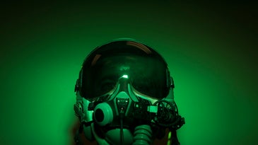 Air Force pilot with 1980's-style helmet and night vision goggles on drenched in green light