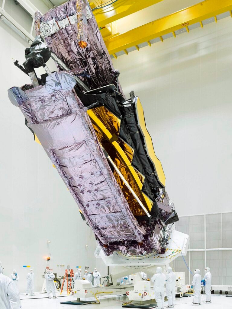 James Webb Space Telescope folded up in an insulated silver wrapping and held on a forklift at a diagonal angle to prep for the rocket