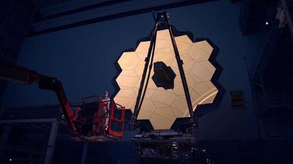 James Webb Space Telescope honeycomb gold-coated primary mirror being cleaned by an engineer in protective clothing on a forklift