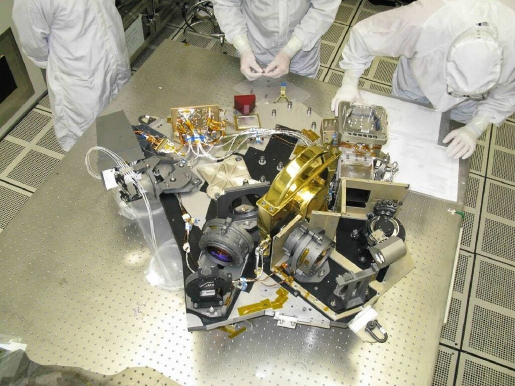 James Webb Space Telescope near infrared camera being tested by three engineers in white protective gear on a metal table