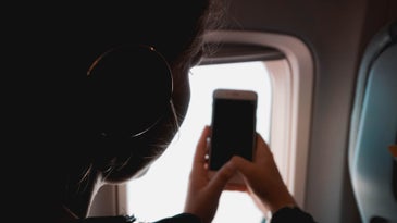 a person looks out a plane window and holds a smartphone