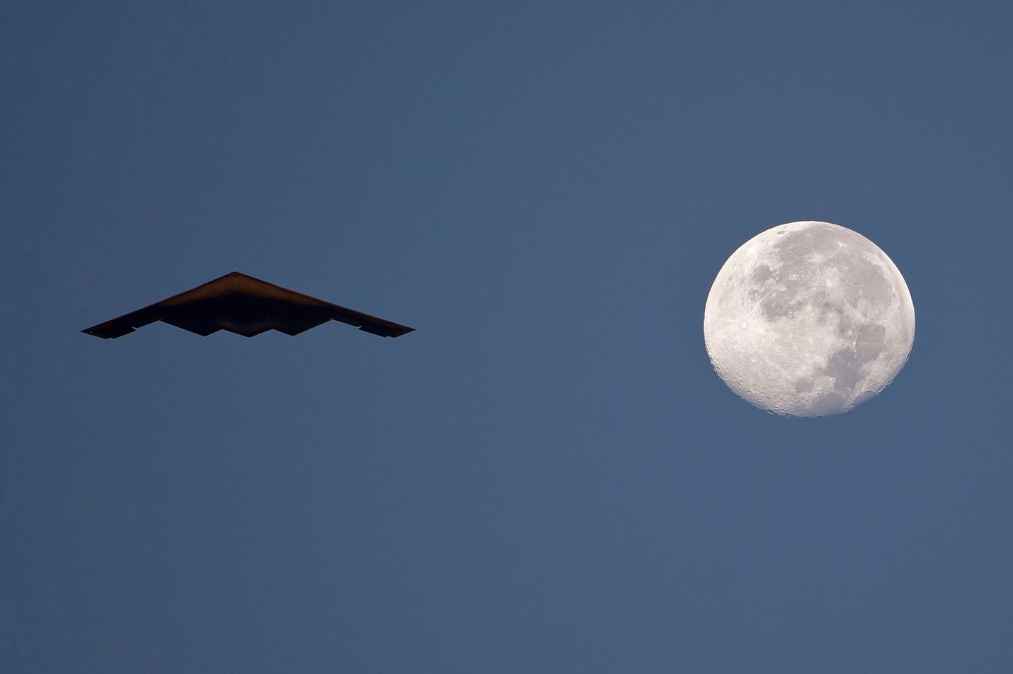 Air Force B-2 Spirit stealth bomber silhouetted next to a full moon