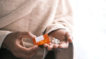 a pair of hands holds an orange medicine bottle and shakes white pills out