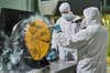 Engineers in protective gear blasting one of the James Webb Space Telescope's gold-coated primary mirrors with white powder