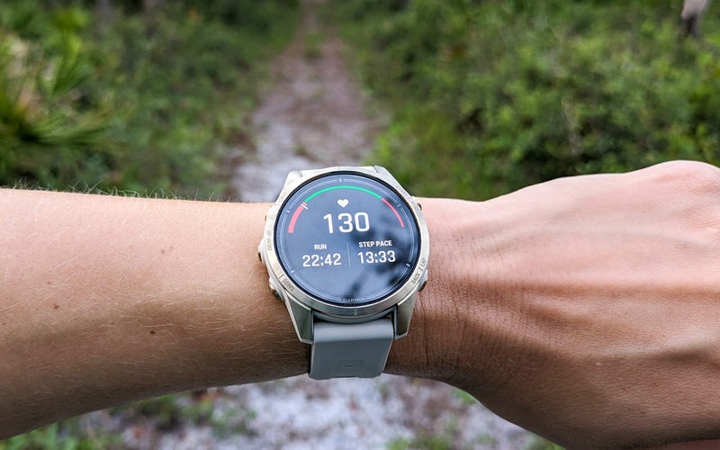 The Garmin epix Pro Sapphire Edition on a wrist in front of a trail displaying running data