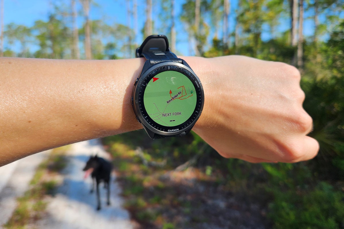 The Garmin Forerunner 965 on a wrist showing a map with a forest and trail in the background