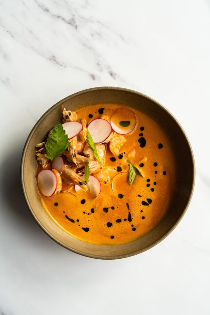 Asian seafood broth or soup with radishes and garnishes photographed from above on a white table