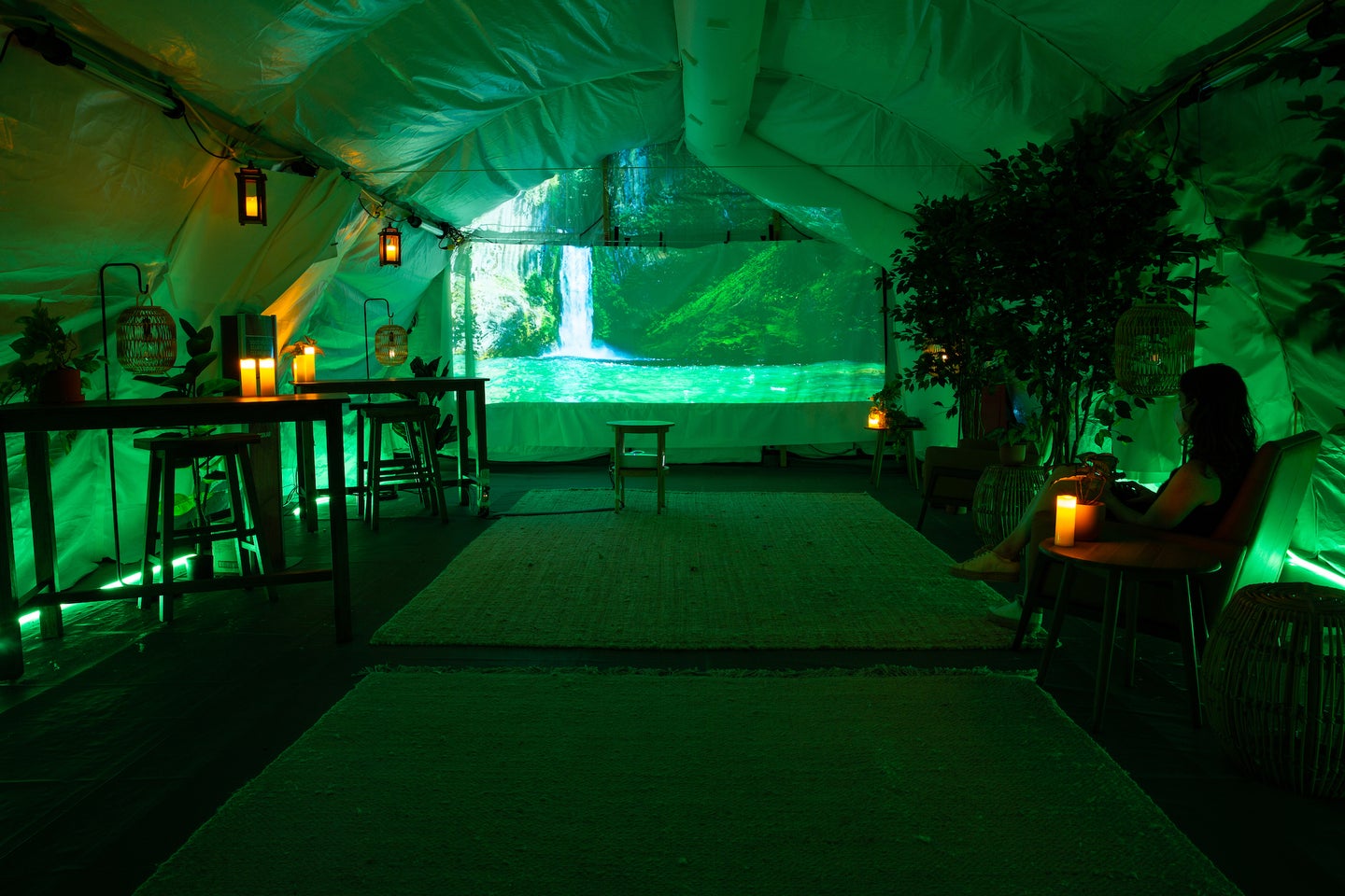 COVID tent filled with green light and a forest scene projected on one wall