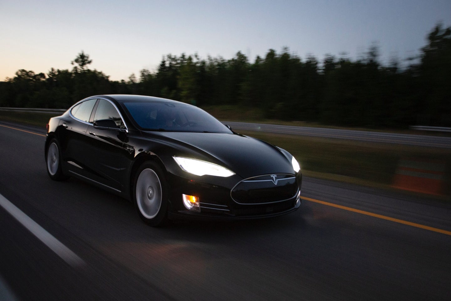 Black Tesla Model S driving on a road at dusk