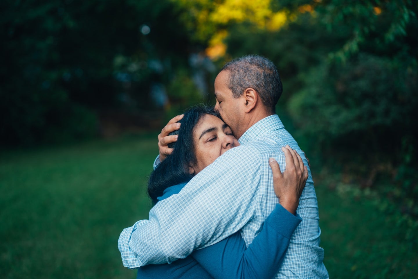 A brown-skinned couple hugging tightly to manage relationship stress in front of trees