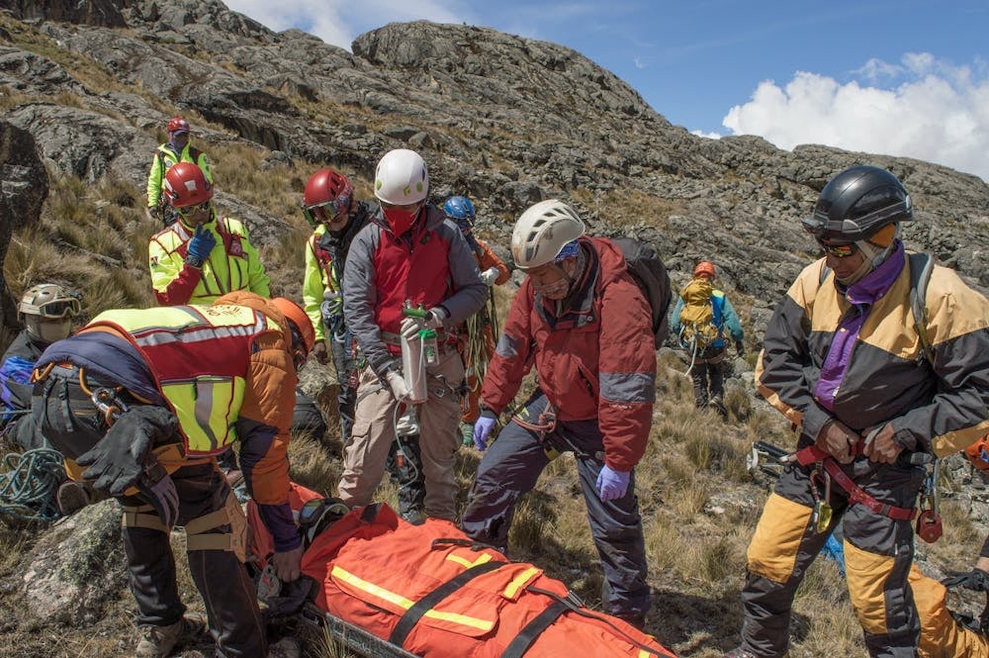 Group of first responders with gear training with an orange body bag on a rocky mountain slope