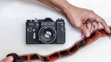Zenit film camera with two hands holding a strip of negatives