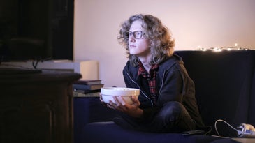 Person watching television with bowl of popcorn.