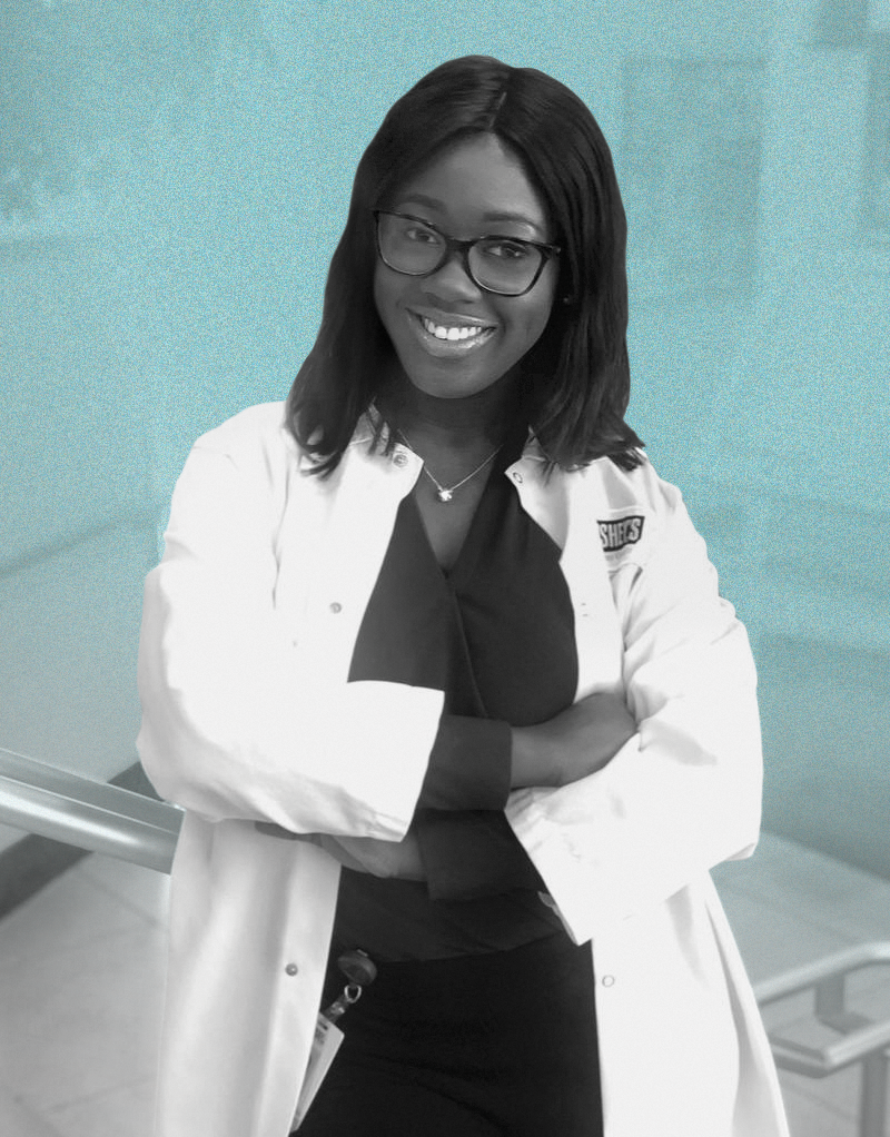 a woman with dark skin and hair wearing a white lab coat smiles at the camera