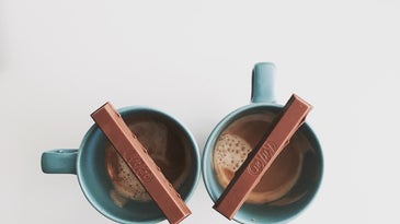 two pieces of a kit kat bar balanced on mugs of hot chocolate