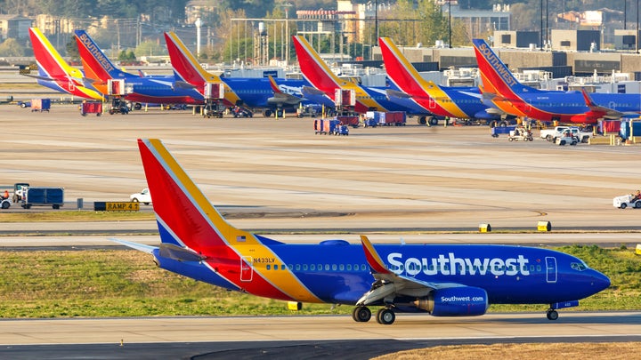 Rows of blue, red, and orange Southwest planes grounded on a domestic airport tarmac because of cancelled flights