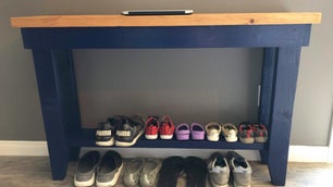A blue wooden shoe rack table against a gray wall with neatly paired shoes on it.