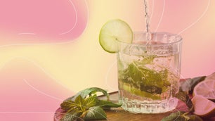 a glass of water with a slice of lemon and mint inside on a pink and yellow background