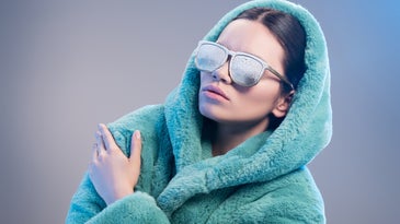 White-skinned person in a furry green robe with frost on face and sunglasses during low wind chill temperatures