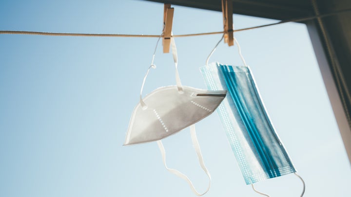 A white COVID respirator mask and blue surgical masks hanging on a clothesline in a window