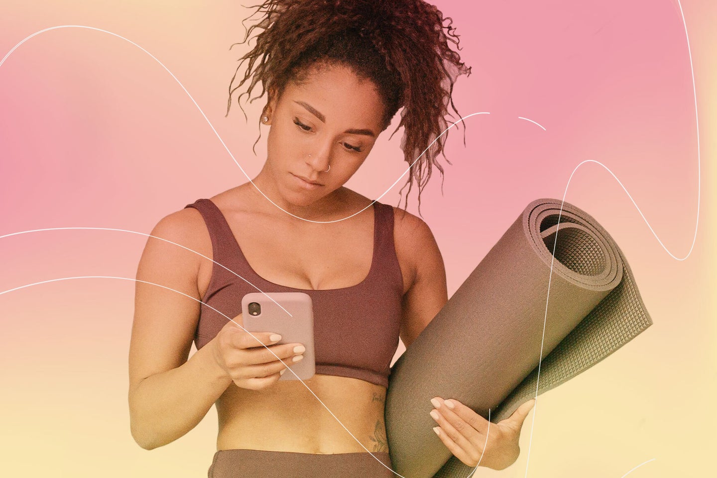 a woman with tan skin and curly hair wearing workout clothes and holding a yoga mat looks down at her phone