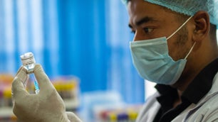 a doctor in a face mask, gloves, and hair net draws a vaccine with a syringe out of a vial
