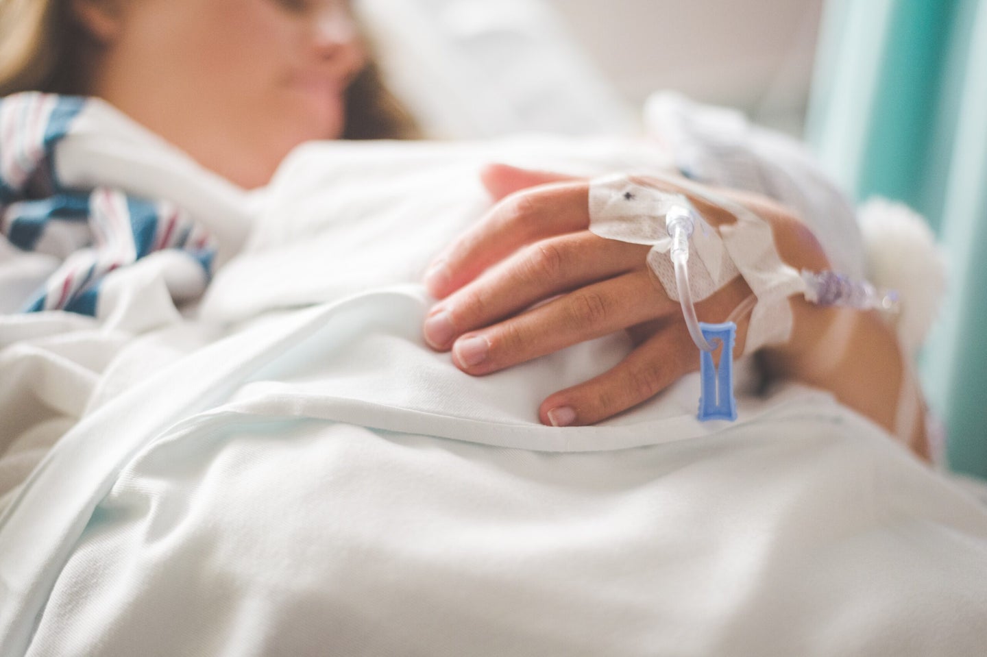 a woman in a hospital bed with a close up on the venous catheter tubes in her hand and arm