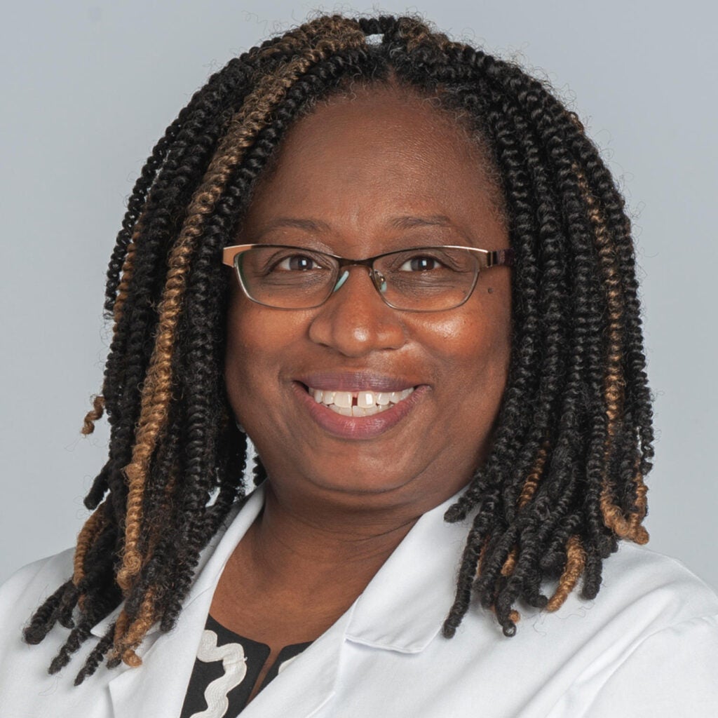 Black doctor in glasses and braids smiling at the camera