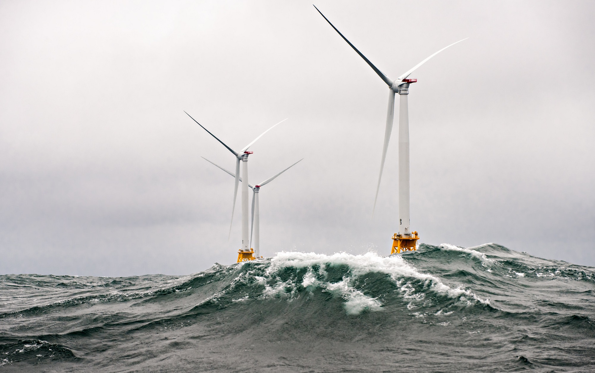 Two wind farm turbines in choppy waves under a stormy sky
