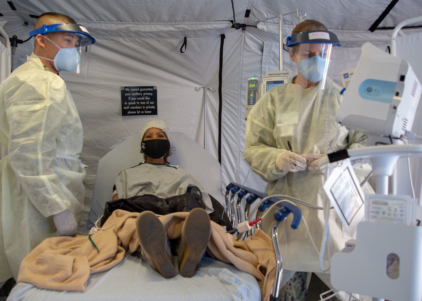 A patient sitting on a hospital bed with an IV, with two medical providers wearing protective clothes on either side.