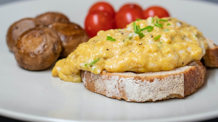 Scrambled eggs on some toast with roasted potatoes and cherry tomatoes on a white place.