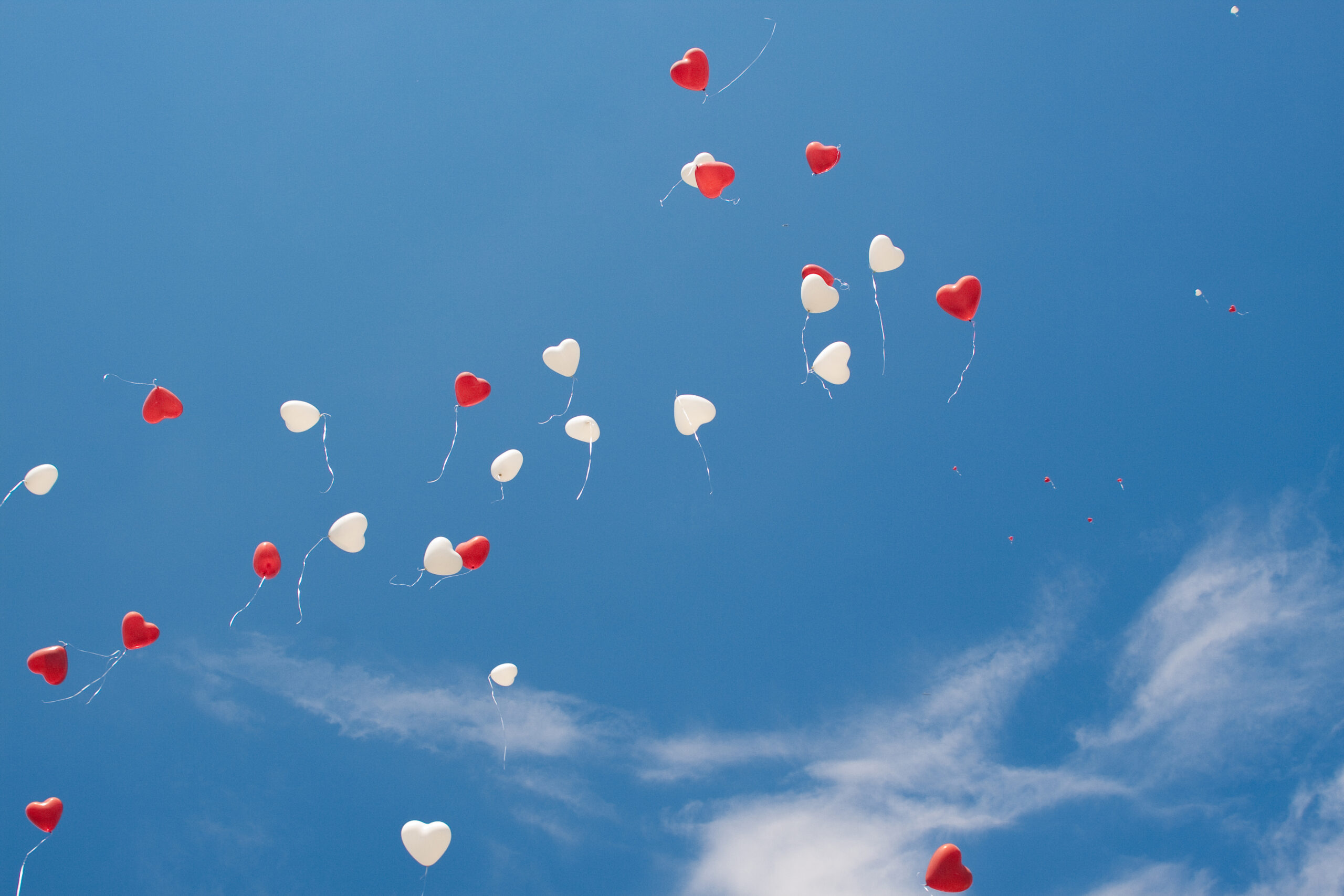 Red and white heart balloons released into blue sky which can become hazardous.