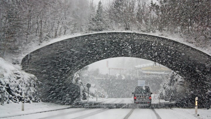 Truck driving under bridge in a blizzard.