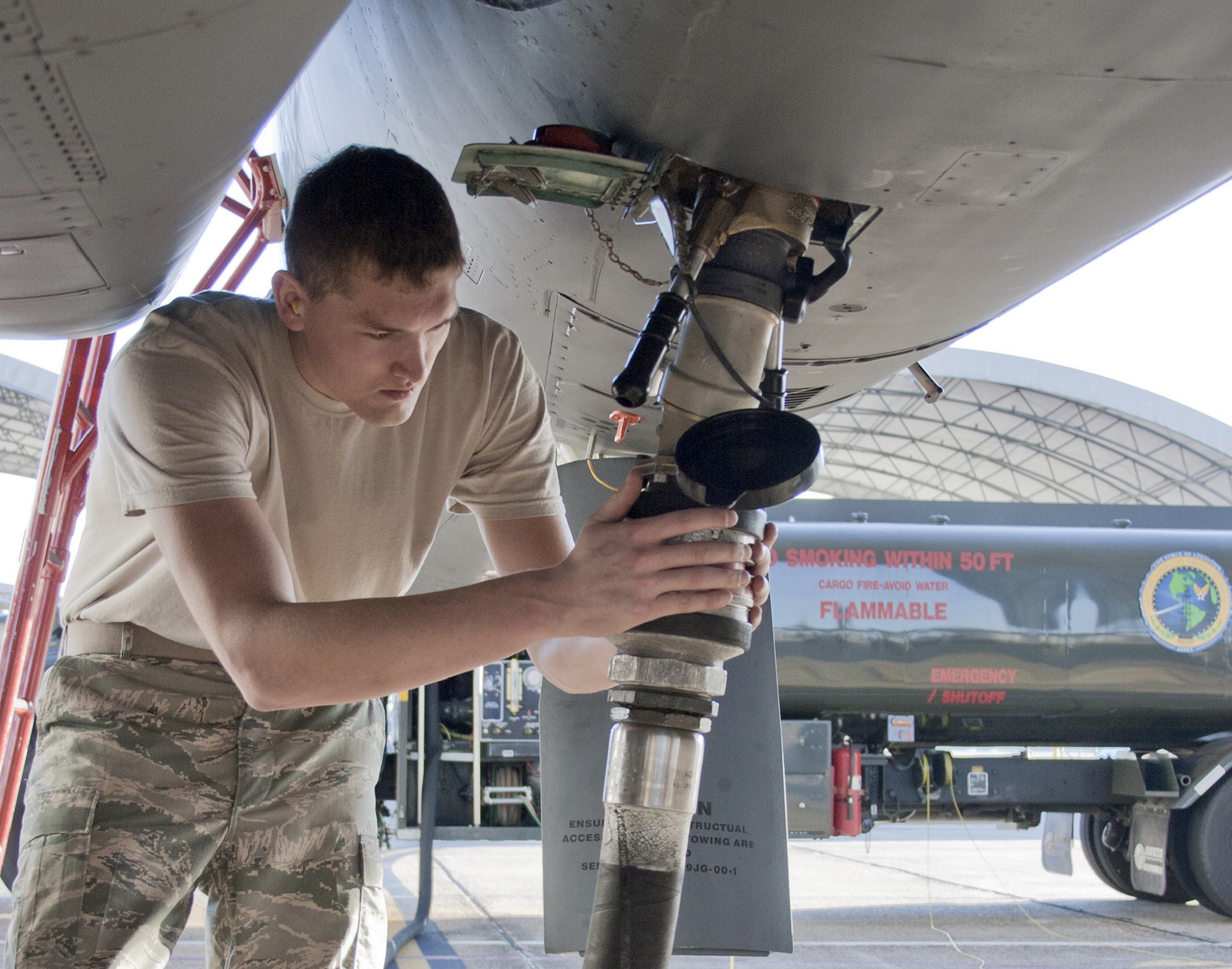 Air Force member in fatigue pants and short brown hair pumping fuel into the belly of a jet