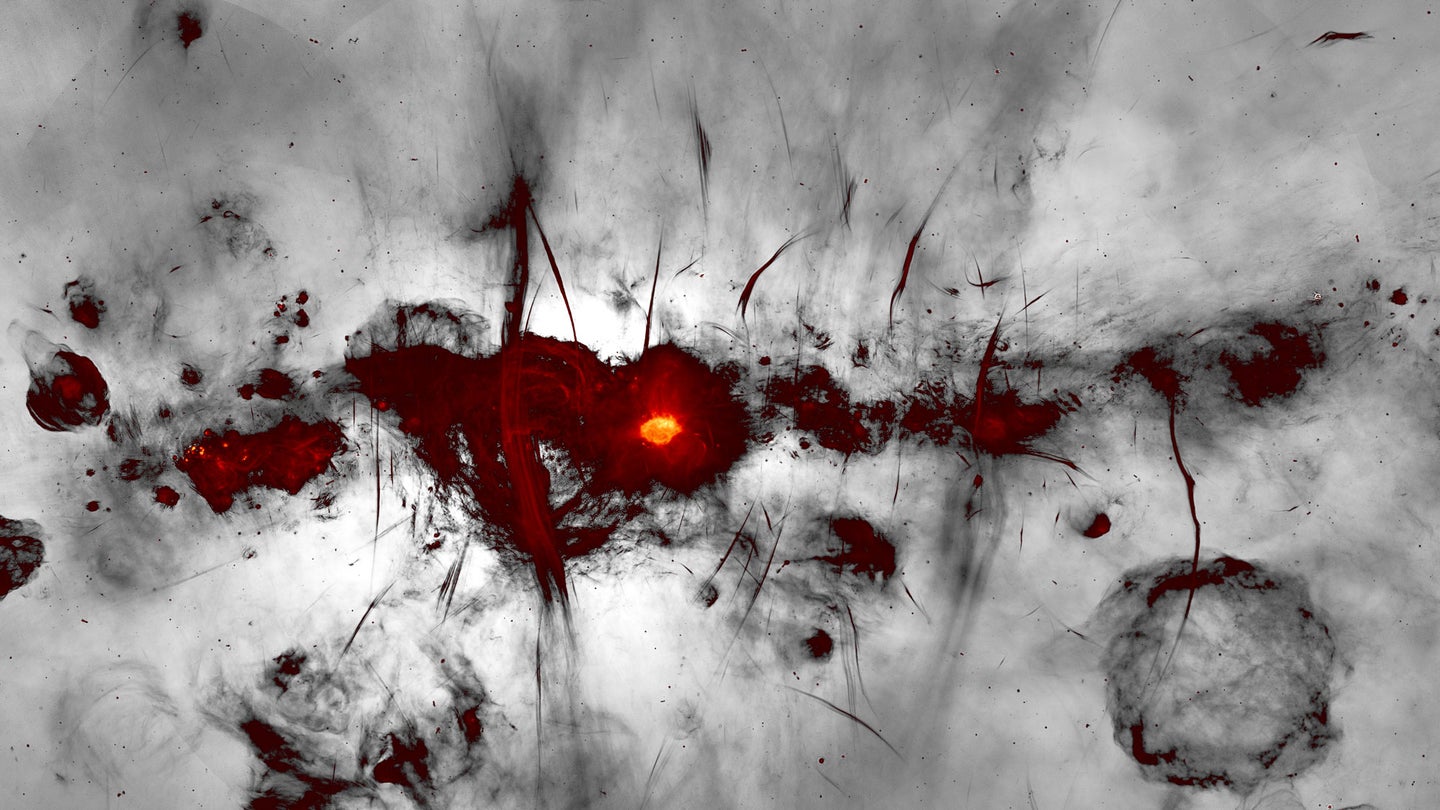 Red, horizontal splotches represent the center of the Milky Way galaxy with a greyscale background. A bright yellow dot represents the black hole at the center.