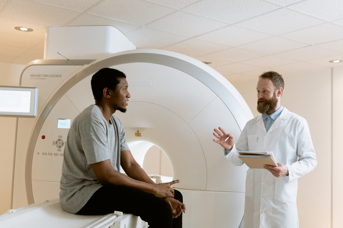 A doctor talks to a patient who is sitting on an MRI machine's bed.