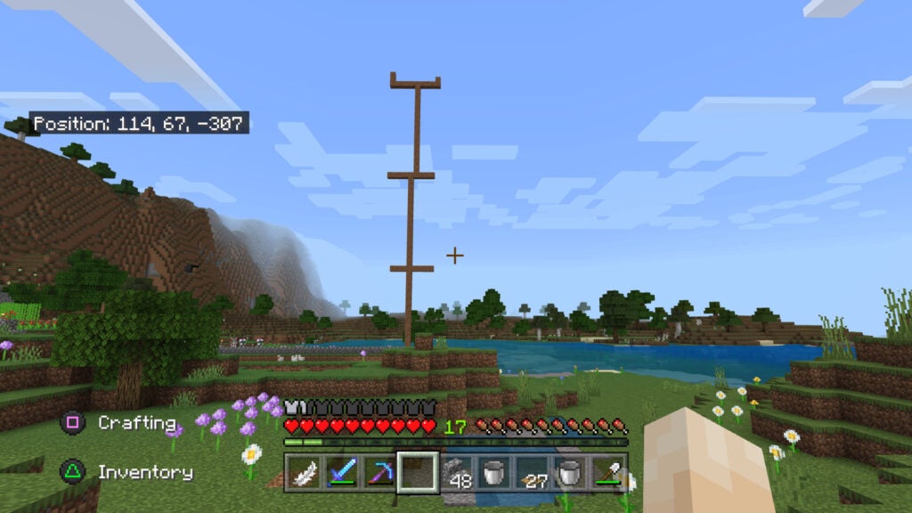 A Minecraft landscape with a tall tower built to serve as a landmark to help the player find their way home, and coordinates displayed to help mark the player's location.