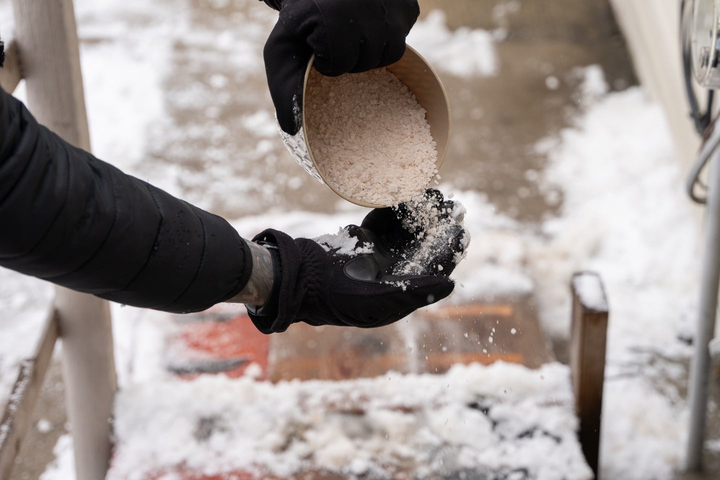 Person with black gloves pouring rock salt over a sidewalk despite environmental pollution