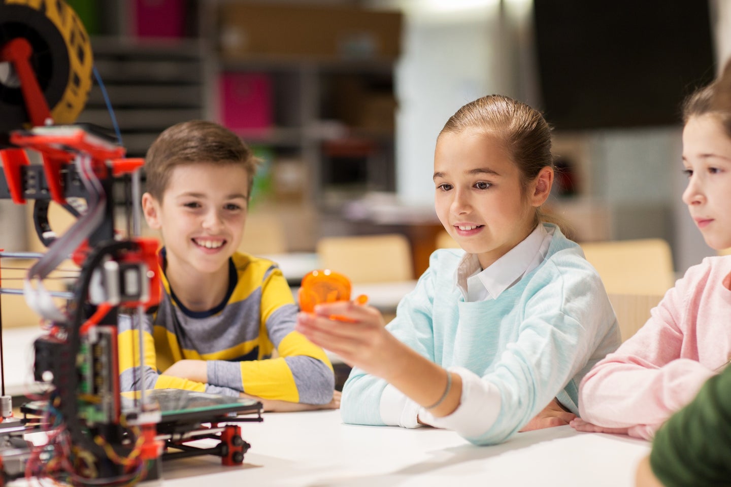 Three excited kids in robotics class printing robot toys on a 3D printer